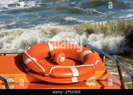 Boa di vita arancione con luce di emergenza per la localizzazione su una barca con un mare accidentato sullo sfondo. Foto Stock