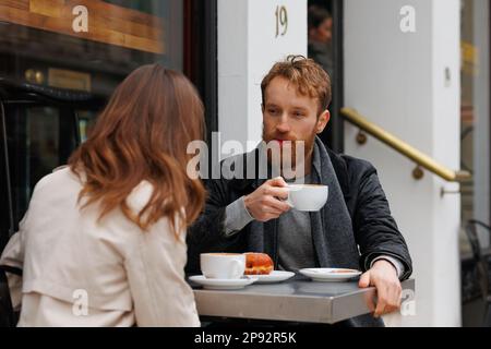 Coppia bevendo caffè e ridendo parlando tra loro seduti al tavolo del caffè all'aperto sulle strade della città Foto Stock