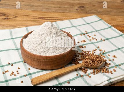 Farina di grano saraceno pila in ciotola di legno, polvere di grano saraceno secco, farina di grano saraceno senza glutine su legno rustico sfondo vista laterale Foto Stock