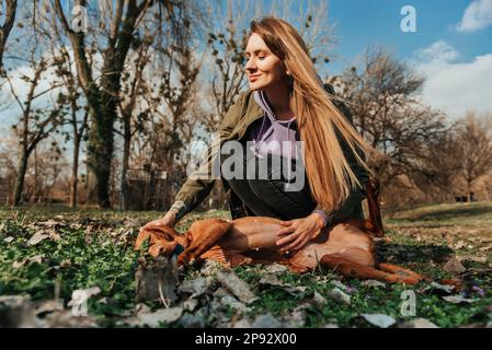 Donna Petting Dog sdraiato a terra nel Parco Foto Stock