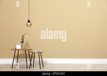 Piccoli tavoli con decor vicino alle pareti beige in camera, spazio per testo. Design degli interni Foto Stock