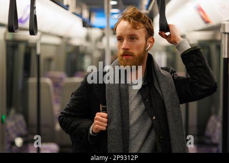Uomo bearded in cuffie wireless e con uno zaino è in piedi in un treno della metropolitana Foto Stock