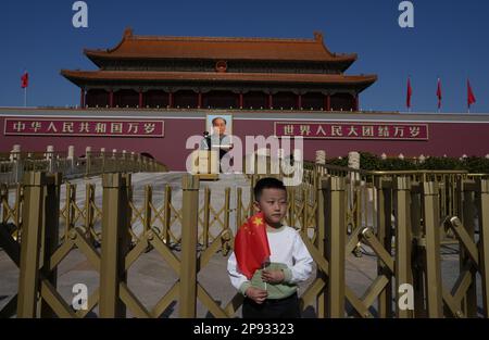 Un ragazzo tiene con la Cina posa bandiera nazionale sotto un ritratto del defunto presidente cinese Mao Zedong vicino polizia e agenti di polizia paramilitare in piedi guardia alla porta Tiananmen, davanti al Congresso nazionale del popolo (NPC) a Pechino, Cina 3 marzo 2023. 03MAR23 SCMP / Robert ng Foto Stock