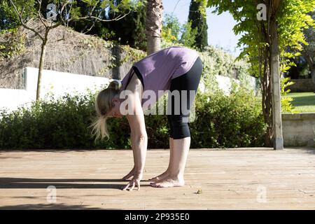 Donna in pre-bend durante la sua pratica di yoga su una terrazza al sole Foto Stock