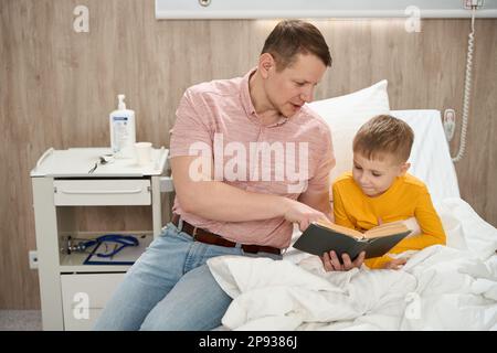 felice padre e figlio sta leggendo il libro insieme nella falce Foto Stock