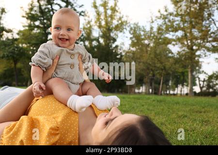 Madre felice con adorabile bambino sdraiato su erba verde nel parco Foto Stock