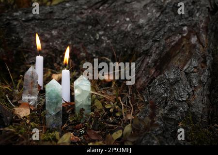 Diversi cristalli e candele brucianti vicino all'albero all'aperto, spazio per il testo Foto Stock