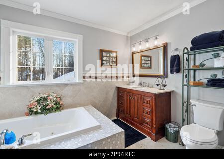 Una vasca da bagno bianca accanto al lavandino del bagno sotto una finestra Foto Stock