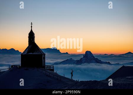 Vista della Wallbergkircherl in direzione di Roßstein, Buchstein e Zugspitze al tramonto d'inverno. Rottach-Egern, Baviera, Germania. Foto Stock