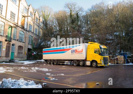 Camion DHL hgv in livrea gialla con rimorchio UKmail collegato parcheggiato all'esterno di una fabbrica di pietra con neve a terra. Foto Stock