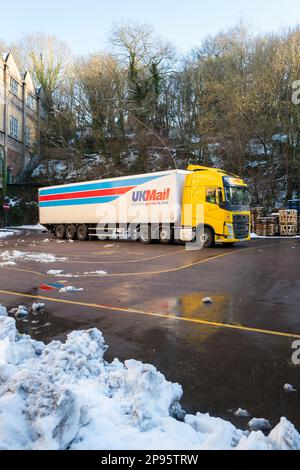 Camion DHL hgv in livrea gialla con rimorchio UKmail collegato parcheggiato all'esterno di una fabbrica di pietra con neve a terra. Foto Stock