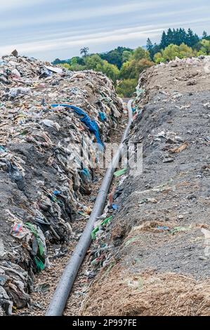 Un tubo perforato per gas metano viene posato in una trincea per essere interrato in una discarica attiva. Foto Stock