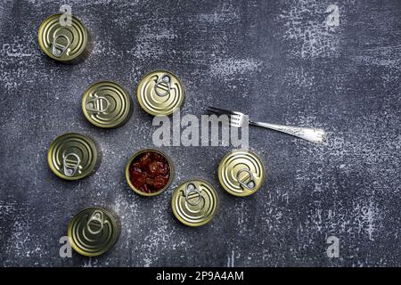 Taniche rotonde di pesce in scatola in salsa con una aperta e una forchetta per svuotarla Foto Stock