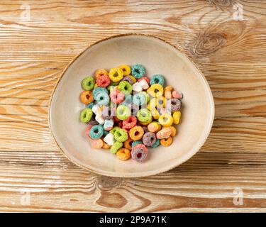 Variopinti anelli per la colazione pile, anse di frutta, anelli di cereali fruttati con marshmallows, cereali di mais colorati su sfondo di legno Foto Stock