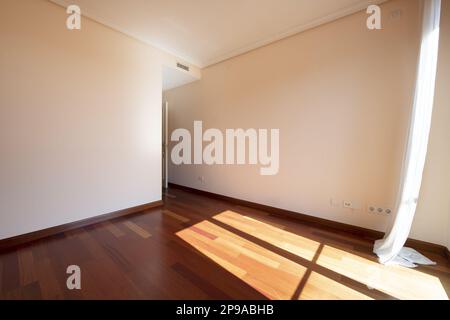 Stanza vuota con pavimenti in parquet rossiccio, un raggio di sole attraverso la finestra una finestra che oscura nel vento Foto Stock