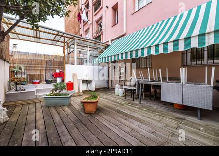 Terrazza patio di una casa al piano terra con alcune piante e pavimenti in legno di acacia non verniciato, bianco e verde tenda bicolore e portico di accesso Foto Stock