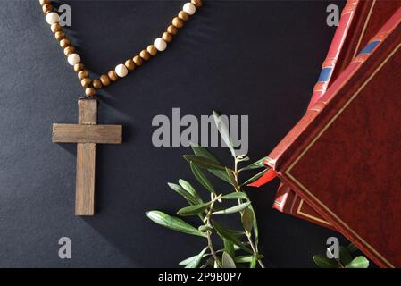 Sfondo religioso pasquale con simboli come libri croce cristiana e rami d'oliva su tavola nera. Vista dall'alto. Foto Stock