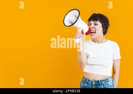 Una donna che fa da sfondo a una parte superiore bianca e jeans che urla in un altoparlante. Sfondo luminoso. Scatto medio. Foto di alta qualità Foto Stock