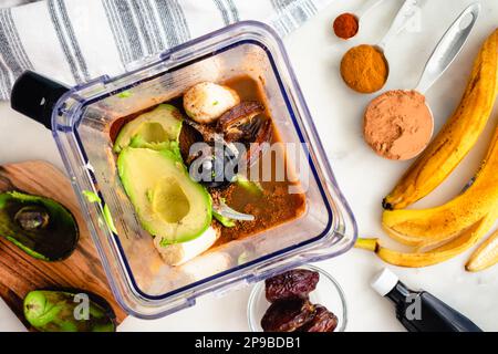 Vista dall'alto del caffè-moka Smoothie ingredienti in un frullatore: Avocado, banana, cacao in polvere, e altri ingredienti frullati in una caraffa frullatore Foto Stock