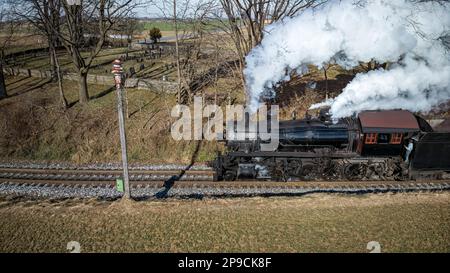 Veduta aerea parallela di un treno a vapore antico restaurato che viaggia attraverso la campagna in un giorno d'autunno soleggiato Foto Stock