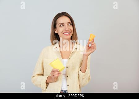 Felice giovane donna con tazza mestruale e tampone monouso su sfondo grigio Foto Stock