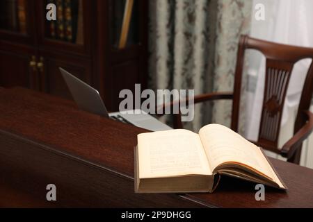 Vecchio libro e computer portatile su un tavolo di legno nella sala lettura biblioteca Foto Stock