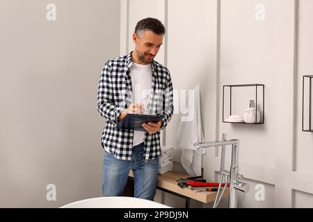 Idraulico con portadocumenti che controlla il rubinetto dell'acqua in bagno Foto Stock