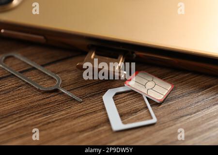 Scheda SIM, telefono cellulare e estrattore su tavolo di legno, primo piano Foto Stock