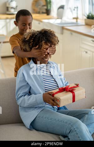 Felice madre afro-americana eccitata che riceve il regalo di giorno delle madri dal bambino Foto Stock