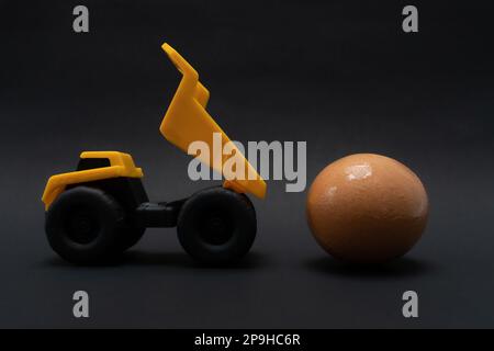 Una foto dopo alcune modifiche, un camion giallo cerca di portare un uovo, su carta di sfondo nera. Foto Stock