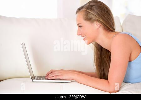 Chattare con gli amici online. una giovane donna attraente che usa un computer portatile mentre si sdraia sul divano. Foto Stock