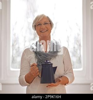 Unisciti a me per una cuppa. Un ritratto corto di una donna anziana felice che tiene una teiera. Foto Stock