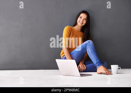 Ive ha tutto ciò di cui ho bisogno proprio qui. Ritratto di una giovane donna attraente seduta sul pavimento con un portatile. Foto Stock