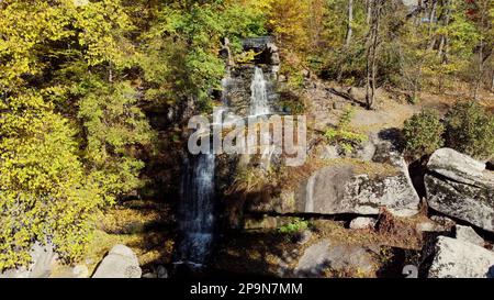 Cascata nel parco autunnale. L'acqua cade da alte pietre, alberi con foglie gialle in parco paesaggio il giorno di autunno soleggiato. Foglie cadute, acqua che scorre, foresta. Paesaggio naturale, paesaggio naturale. Antenna Foto Stock