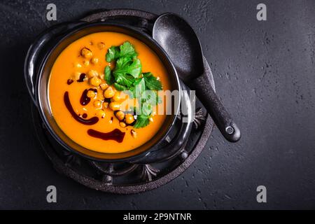 Zuppa cremosa di crema di zucca con olio di semi di zucca, ceci al forno e coriandolo Foto Stock