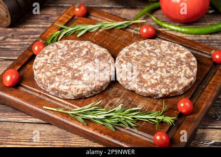 Polpette di hamburger crudi. Hamburger di manzo polpette preparate con spezie. Hamburger di manzo tritati sul tagliere. Foto Stock