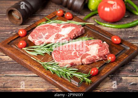 Il manzo ha obbedito. Due bistecche fresche di ribeye crude con spezie e rosmarino. Entrecote speciale. sfondo di legno Foto Stock