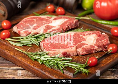 Il manzo ha obbedito. Due bistecche fresche di ribeye crude con spezie e rosmarino. Entrecote speciale. sfondo di legno. Primo piano Foto Stock