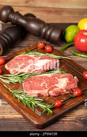 Il manzo ha obbedito. Due bistecche fresche di ribeye crude con spezie e rosmarino. Entrecote speciale. sfondo di legno Foto Stock