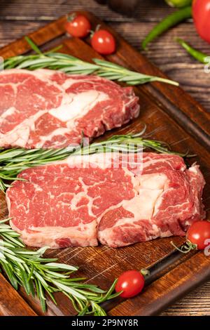 Il manzo ha obbedito. Due bistecche fresche di ribeye crude con spezie e rosmarino. Entrecote speciale. sfondo di legno. Primo piano Foto Stock