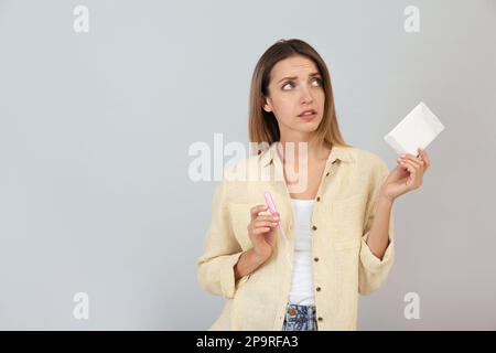 Giovane donna premurosa con tampone mestruale monouso e tampone su sfondo grigio Foto Stock