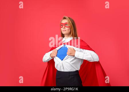 Donna d'affari sicura che indossa il costume di supereroe sotto il vestito su sfondo rosso Foto Stock