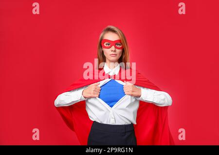 Donna d'affari sicura che indossa il costume di supereroe sotto il vestito su sfondo rosso Foto Stock