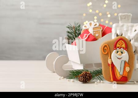 Composizione con gustosi biscotti di pan di zenzero su un tavolo di legno bianco contro le luci sfocate, spazio per il testo. St Festa di Nicholas Day Foto Stock