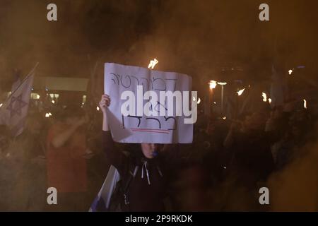 TEL AVIV, ISRAELE - MARZO 9: Un manifestante sostiene un segno che recita "democrazia o ribellione" come manifestanti anti anti-governativi che detengono torce fiammeggianti e lanciano bombe a fumo durante una manifestazione contro il piano di sistema giudiziario del governo di estrema destra di Israele, che mira a indebolire la Corte suprema del paese il 9 marzo 2023 a Tel Aviv, Israele. Foto Stock