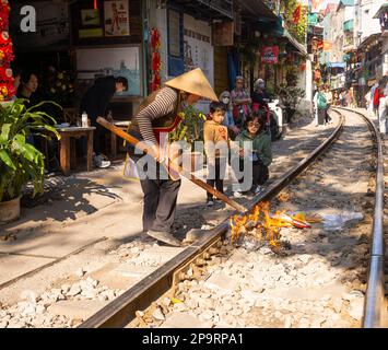 Hanoi, Vietnam. Jnauary 2023. Una donna che brucia tiền âm phủ, offerte votive per gli antenati lungo i binari del treno di fronte alla sua casa nel vecchio quarto Foto Stock