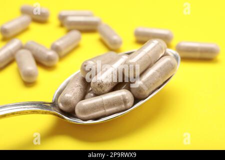 Capsule di gelatina in cucchiaio su fondo giallo, primo piano Foto Stock