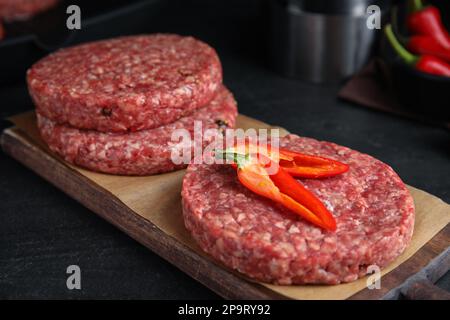 Polpette di hamburger crudi con peperoncino su tavola nera, primo piano Foto Stock