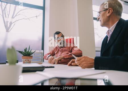 Primo piano di due uomini d'affari più anziani che hanno una conversazione mentre si siedono nello spazio di lavoro del co Foto Stock