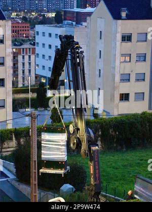 I pannelli di vetro sono consegnati al tetto piano di un blocco di appartamenti da una gru a distanza montata su autocarro al crepuscolo Santander Cantabria Spagna Foto Stock